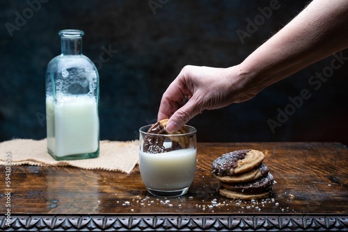 Closeup shot of a person putting the cookie in a glass of milk