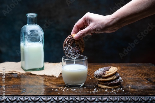 Closeup shot of a person putting the cookie in a glass of milk