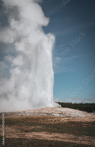 Errupting Old Faithful Geyser in Yellowstone National Park, Wyoming, USA. Travel and adventure concept. Blue sky and sunny day.