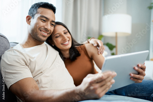 Just us and our favourite movie. a young couple sitting on the sofa together at home and using a digital tablet.