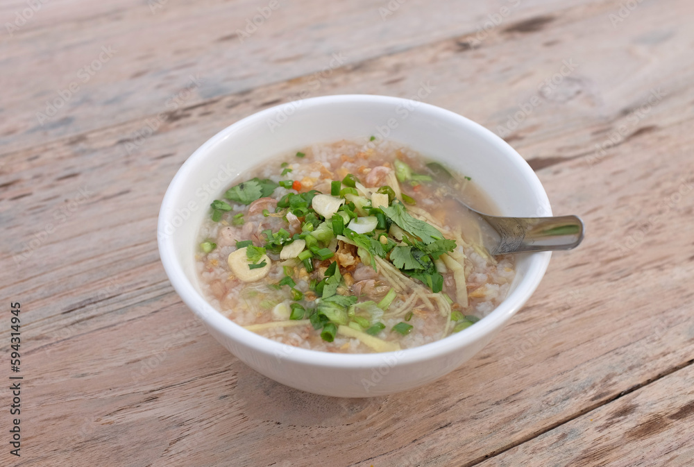 Rice porridge with minced pork, garlic, coriander, chili, spring onion and ginger in white bowl against wood table background. Rice porridge with minced pork, garlic, coriander, chili, spring onion and ginger in white bowl against wood table background.