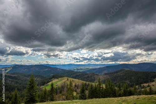 View of green hills with lush woods against the background of the cloudy sky.