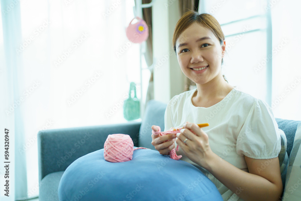 Happy cheerful Asian woman doing a crochet in living room in free time. Skillful Asian craftswoman knitting a handcraft crochet sweater and hat in cozy living room. Happy cheerful Asian woman doing a crochet in living room in free time. Skillful Asian craftswoman knitting a handcraft crochet sweater and hat in cozy living room.