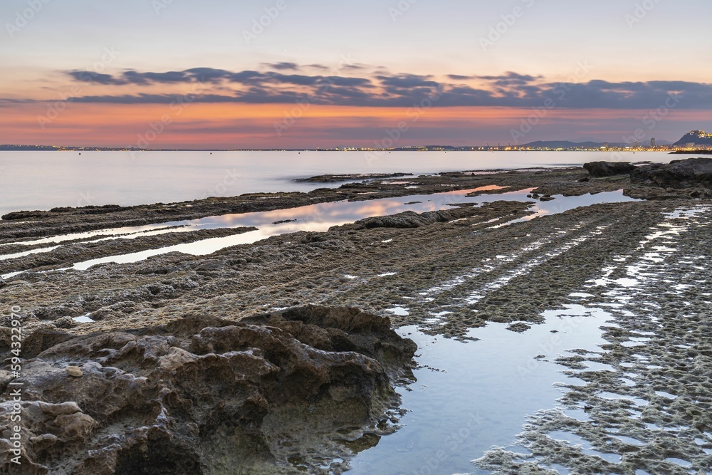 Scenic view of a shoreline featuring a rocky beach and a vast blue ocean at sunset