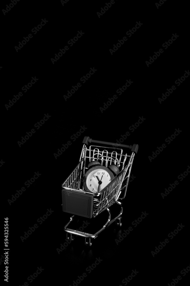 Alarm clock in a shopping cart on a black background.Shopping time. Alarm clock in a shopping cart on a black background.Shopping time.