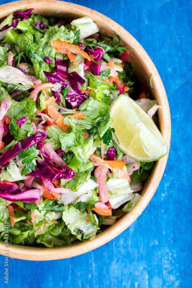 Fresh vegetable salad with purple cabbage, white cabbage, lettuce, and carrot, in a wooden bowl on a blue wooden background. Top view. Fresh vegetable salad with purple cabbage, white cabbage, lettuce, and carrot, in a wooden bowl on a blue wooden background. Top view.