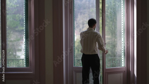 Back view of person opening large windows and stepping out to home balcony enjoying fresh air and standing in contemplation