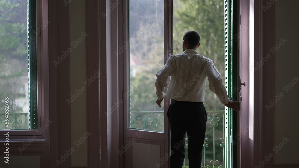 Back view of person opening large windows and stepping out to home balcony enjoying fresh air and standing in contemplation