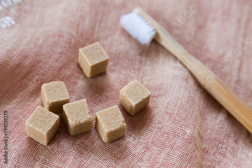 Selective focus flat lay view of brown sugar cubes next to toothbrush on linen background