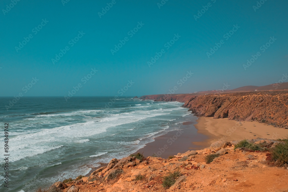 Rugged cliffside view of Aftas Beach and Atlantic Ocean in the chill coastal town of Mirleft, Morocco. Landmark popular with surfers, locals, and tourists. Travel day background. Beautiful landscape.