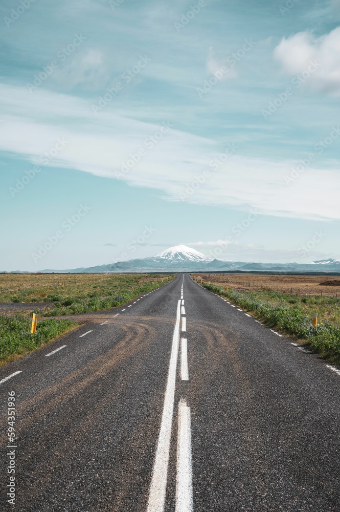 Vertical shot of a  scenic, empty roadway leads to the Hekla mountain range on a partly cloudy day
