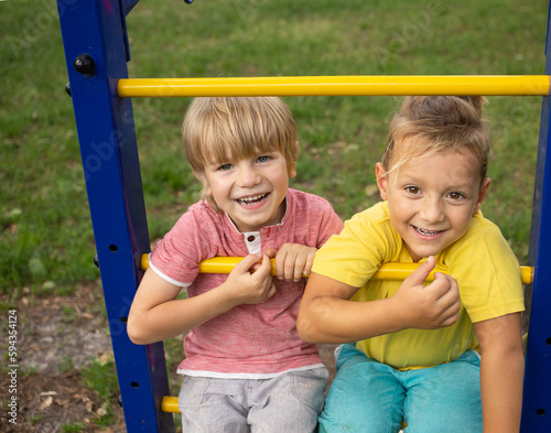 two 5-year-old boys are cute smiling while sitting on the playground in summer. Happy childhood, positive emotions, friendship of children, joy of communication