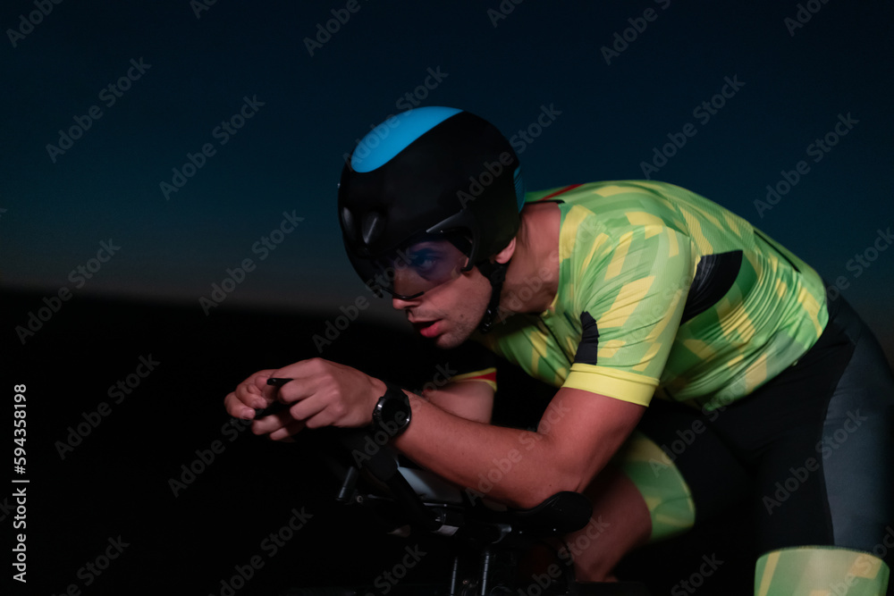 A triathlete rides his bike in the darkness of night, pushing himself to prepare for a marathon. The contrast between the darkness and the light of his bike creates a sense of drama and highlights the A triathlete rides his bike in the darkness of night, pushing himself to prepare for a marathon. The contrast between the darkness and the light of his bike creates a sense of drama and highlights the