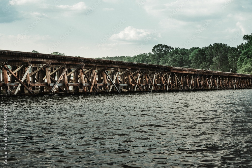 Weathered train bridge spanning a body of water under the cloudy blue sky