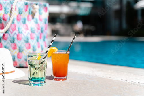 Sticker Tropical sparkling lemonade cocktails by the pool with pink beach bag and white hat in the background