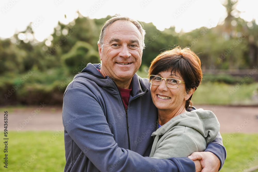 Happy senior couple hugging each other at city park while smiling on camera - Joyful elderly and love concept