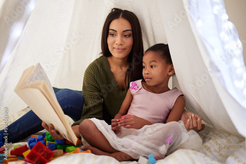 Spark your childs imagination through stories. a mother reading a book to her little daughter under a blanket fort at home.