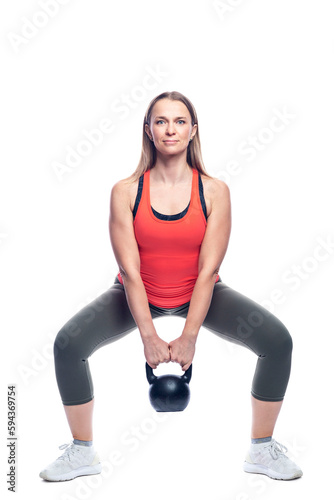 A woman in bright sportswear squats with a kettlebell. Health and active lifestyle. Isolated on white background. Full height. Vertical.