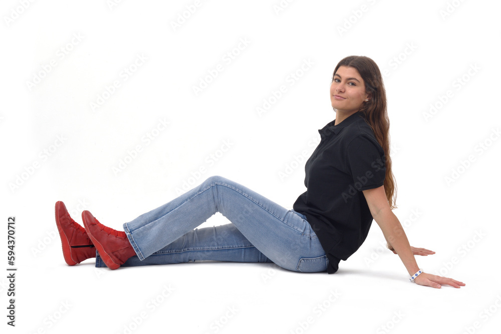 side view of a young girl sitting on the floor with straight legs and looking at camera on white background