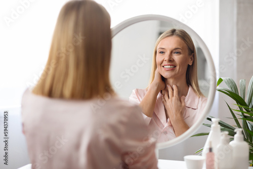 Self-Care Concept. Attractive Middle Aged Female Looking At Mirror At Home