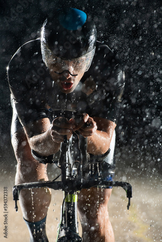 A triathlete braving the rain as he cycles through the night, preparing himself for the upcoming marathon. The blurred raindrops in the foreground and the dark, moody atmosphere in the background add