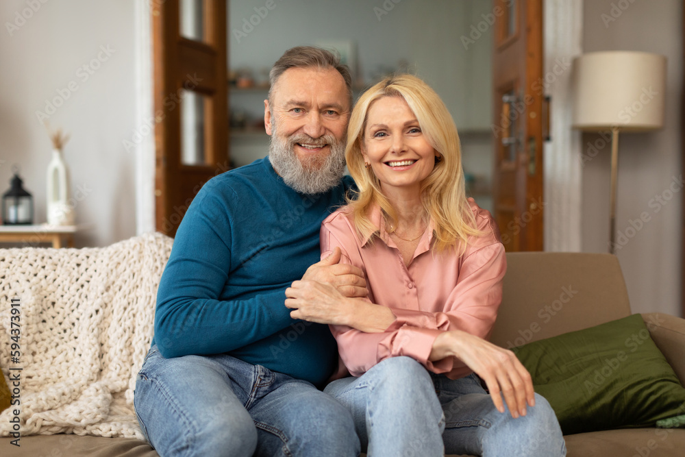 Happy European Couple Embracing Sitting Smiling To Camera At Home