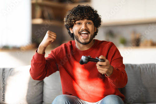 Emotional indian guy playing video game with joystick at home