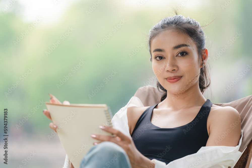 Portrait of young Asian woman holding to writing notebook at home, Smiling and laying to writing in a book, happy young girl relaxing to education outdoor garden, free time hobby and relax concept. Portrait of young Asian woman holding to writing notebook at home, Smiling and laying to writing in a book, happy young girl relaxing to education outdoor garden, free time hobby and relax concept.
