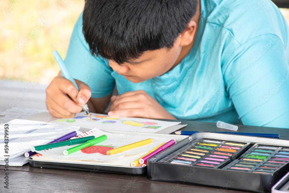 Asian boy spending his free times with drawing, sketching, coloring by using watercolor in the backyard of his house area, soft and selective focus, teenagers activity in summer concept. Asian boy spending his free times with drawing, sketching, coloring by using watercolor in the backyard of his house area, soft and selective focus, teenagers activity in summer concept.