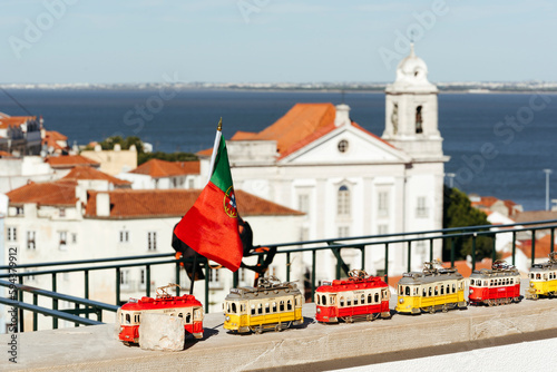 Traditional souvenirs in form of trams on tourist street in Lisbon Portugal on ancient architecture and blue ocean on sunny day. Travel background.