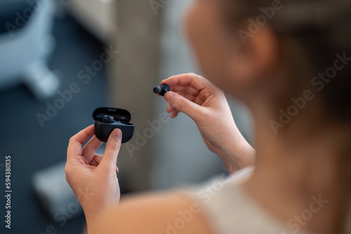 Close up photo over woman's shoulder of woman's hands holding black earphones. Unrecognizable fitness woman holding in-ear headphones. Sportswoman taking modern earphones out of the charging case box.