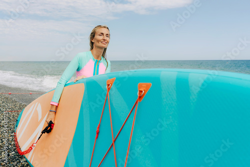 A young woman carries a SUP board to the sea and smiles. photo