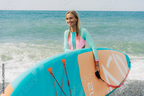 Happy smiling young woman carries sup board into the sea.