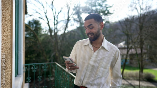 One Happy Arab young man looking at smartphone device screen standing at balcony. A Middle Eastern person receiving positive message on cellphone © Marco