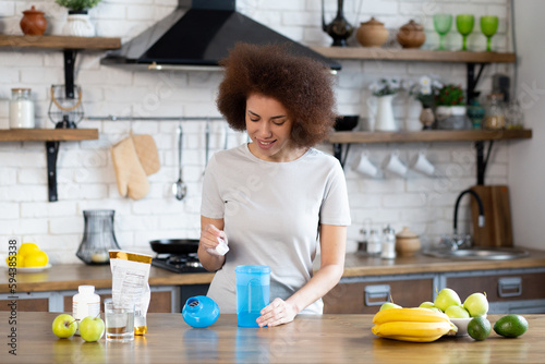 Young sporty african american woman pouring protein powder into a cup to make replacement food meal after workout