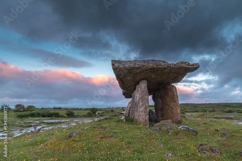 Ancient portal thomb Poulnabrone Dolmen standing on green grass in a rocky field in Glenslane Ireland just before sunset with a background of blue clouded sky photo