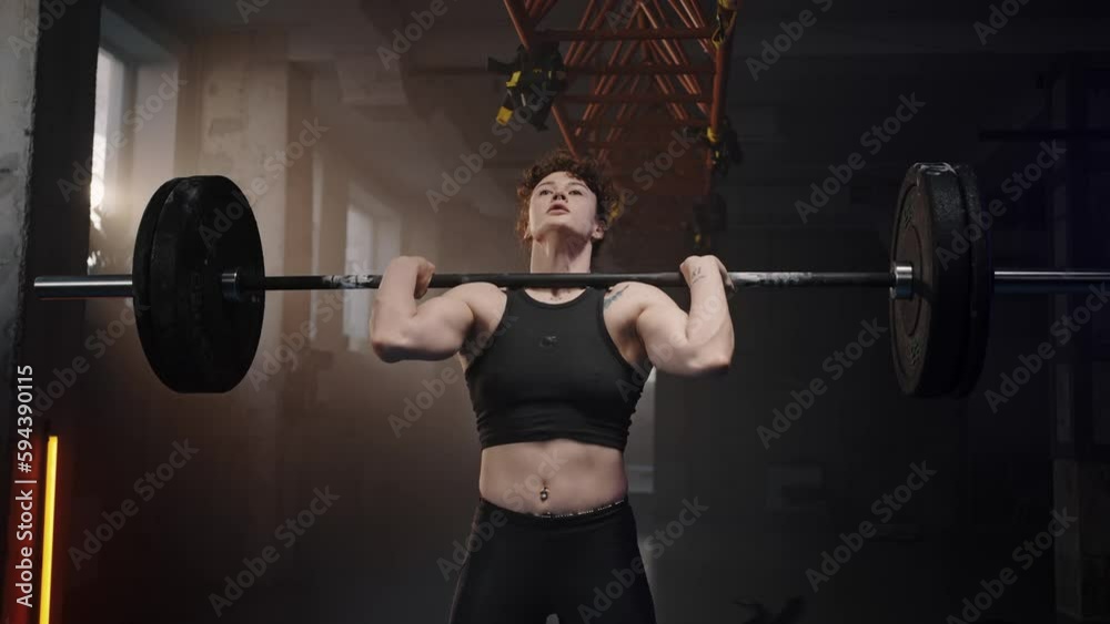 Sporty strong woman lifting barbell with extremely heavy weights during weightlifting workout in gym