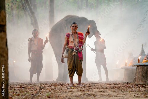 Mahout teacher hold torch and stand in front of other mahout and elephant in concept of traditional ceremony. photo