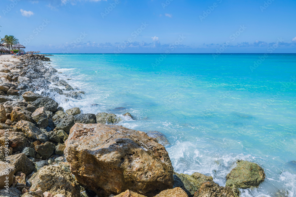 Beautiful view of Atlantic Ocean with turquoise water on island of Aruba with incoming wave on rocky shore.