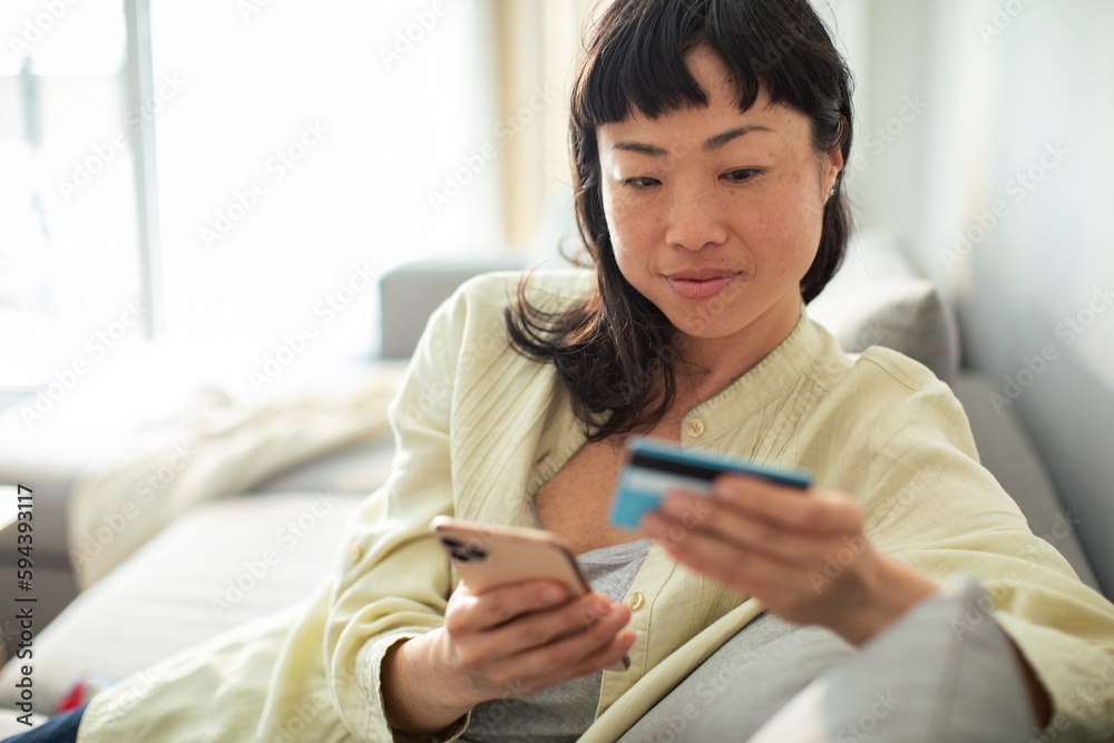 Young Japanese woman online shopping on her smart phone from the comfort of her couch Young Japanese woman online shopping on her smart phone from the comfort of her couch