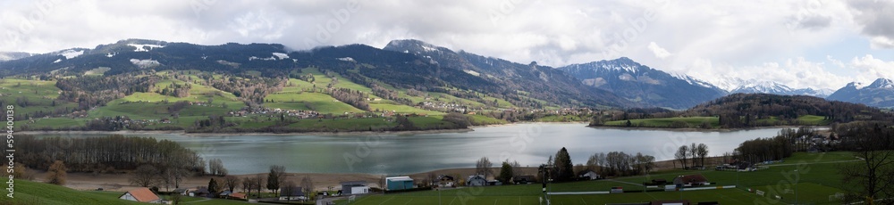 Panoramic picture of a mountainous landscape in Switzerland covered with snow and partly in the clouds with Greyerzersee