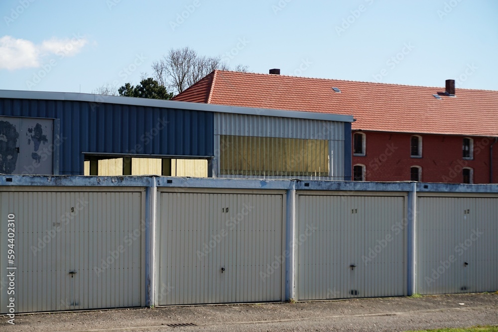 Reihe weißer alter Garagentore vor Fabrikhalle und rotem alten Backsteinhaus bei Sonne am Mittag im Frühling Reihe weißer alter Garagentore vor Fabrikhalle und rotem alten Backsteinhaus bei Sonne am Mittag im Frühling