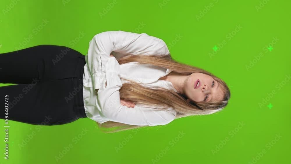 Front view of attractive, young lady standing, posing in studio. Pretty, blonde woman looking at camera tired, crossing hands, waiting, Isolated on green studio background. Front view of attractive, young lady standing, posing in studio. Pretty, blonde woman looking at camera tired, crossing hands, waiting, Isolated on green studio background.