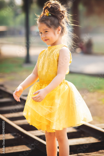 beautiful junior little girl playing in the park in yellow dress laughing with bubbles, screaming with happiness in family enjoying children's day