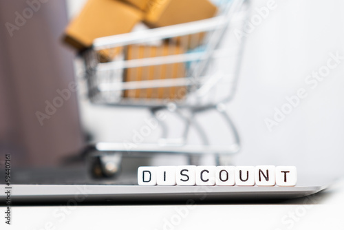 Discount word on cubes with a toy shopping cart and cardboard boxes in the background. Online shopping concept. 