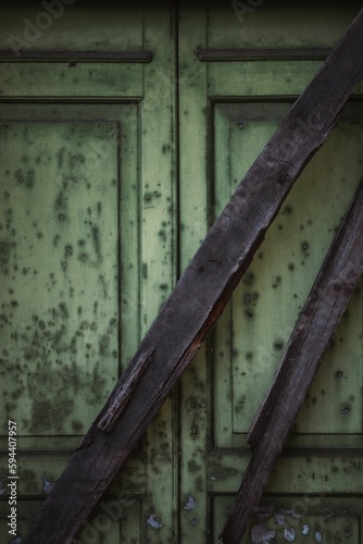 Image features a weathered green door with two rusty wooden bars