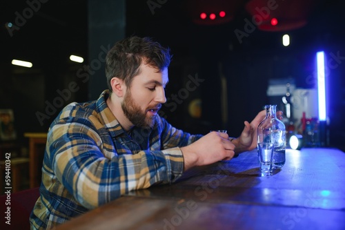 Sad young man sitting at bar counter in pub. Upset man drinks alcohol because of problems at work.