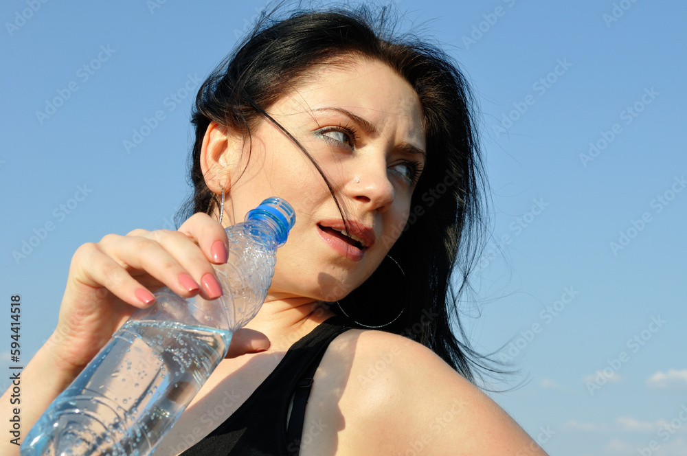 young attractive woman drinks cold water in hot day on blue sky background young attractive woman drinks cold water in hot day on blue sky background