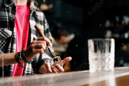 The bartender breaks the ice Close-up of male hands cracking ice with a sharp tool in a bar