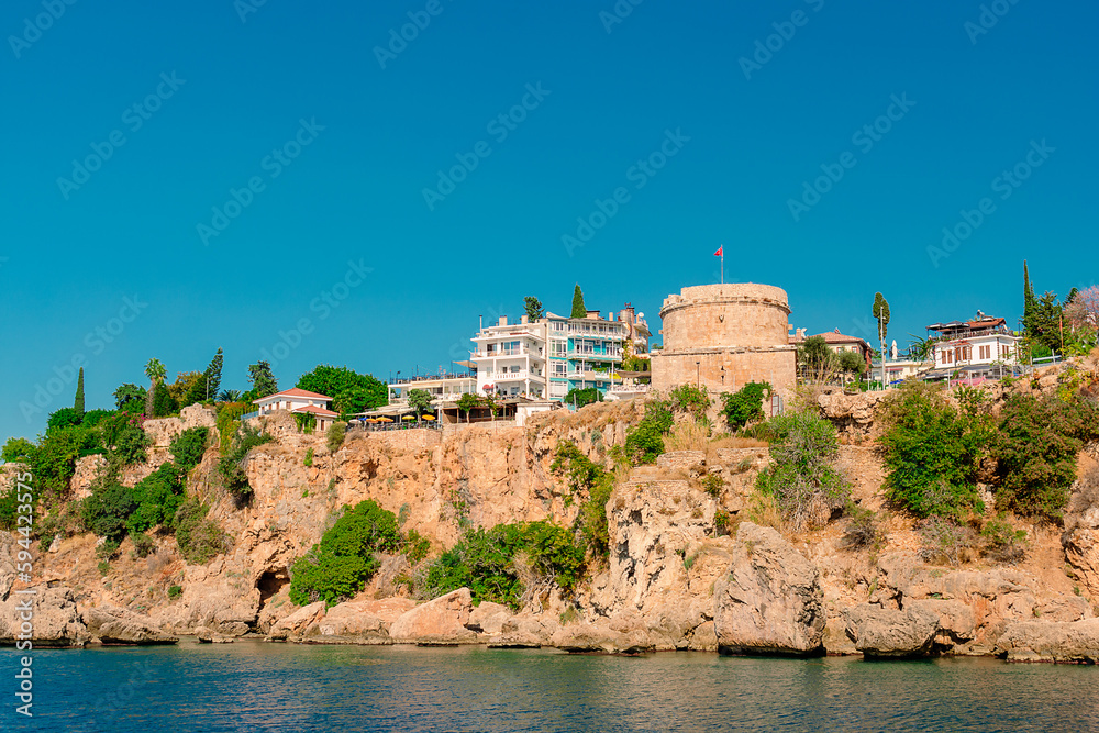 View of the rocky coast with a tower and modern buildings on it from the sea in the city of Antalya.